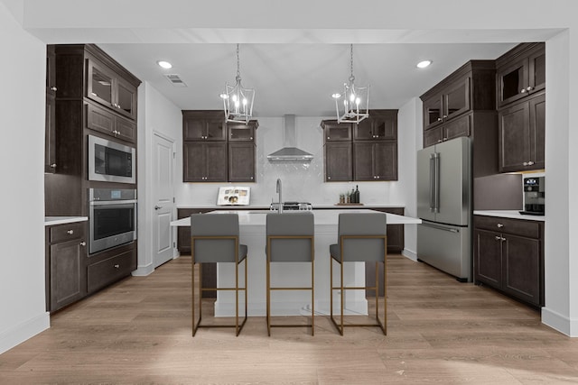 kitchen with light wood-type flooring, stainless steel appliances, wall chimney exhaust hood, and a sink