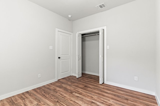 unfurnished bedroom featuring a closet, visible vents, baseboards, and wood finished floors