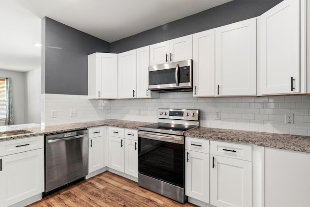 kitchen with tasteful backsplash, white cabinets, appliances with stainless steel finishes, and light wood finished floors