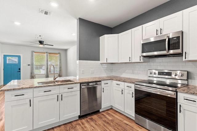 kitchen featuring a peninsula, visible vents, appliances with stainless steel finishes, a sink, and light wood finished floors