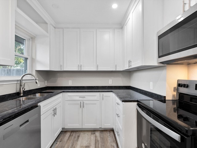 kitchen with dark stone countertops, a sink, appliances with stainless steel finishes, white cabinetry, and light wood-type flooring