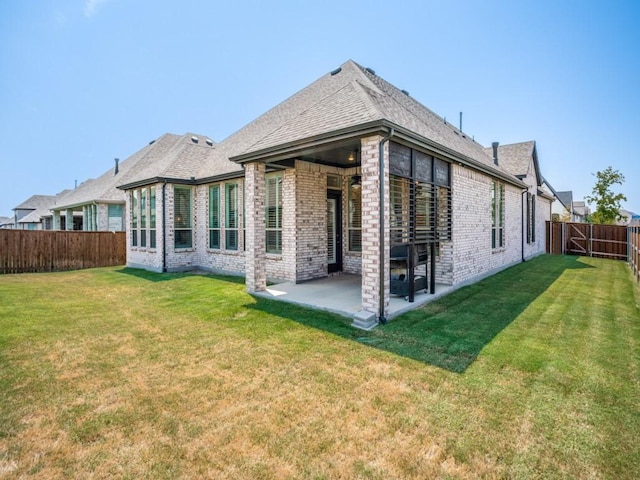 rear view of property featuring a yard, a patio, brick siding, and a fenced backyard