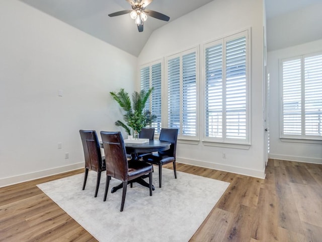 dining room featuring baseboards, light wood-style flooring, a ceiling fan, and vaulted ceiling