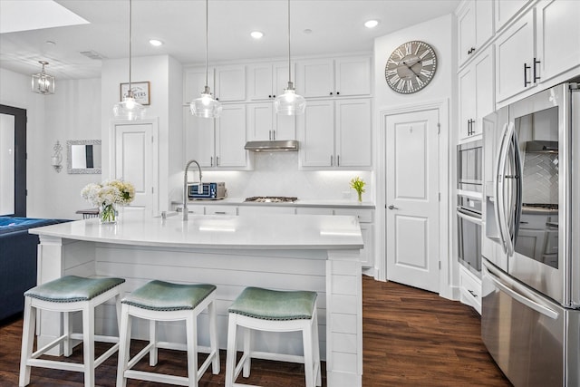 kitchen with dark wood-type flooring, under cabinet range hood, appliances with stainless steel finishes, white cabinets, and light countertops