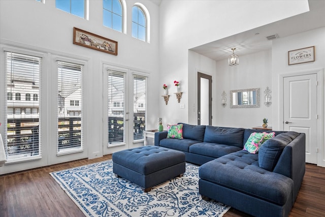 living room featuring a notable chandelier, visible vents, a high ceiling, and wood finished floors