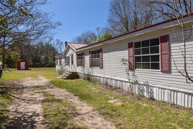 view of side of home featuring driveway, entry steps, an outdoor structure, a lawn, and metal roof