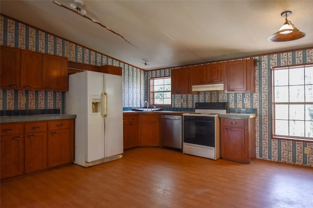 kitchen featuring under cabinet range hood, white appliances, wallpapered walls, and brown cabinetry