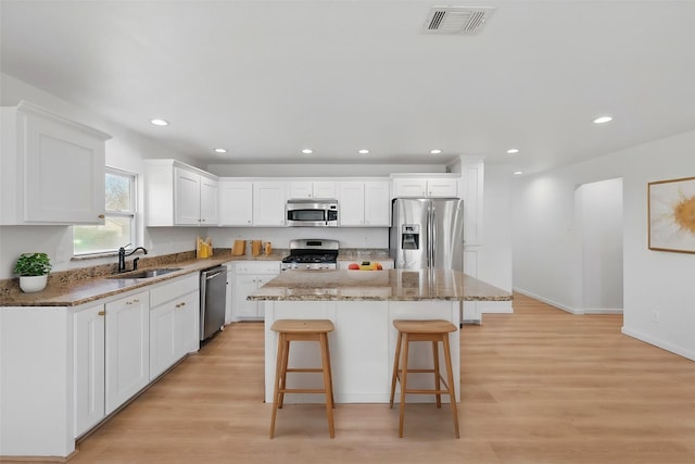 kitchen with visible vents, a kitchen island, appliances with stainless steel finishes, a kitchen breakfast bar, and a sink