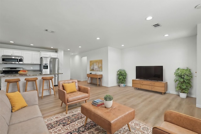 living room with recessed lighting, visible vents, baseboards, and light wood finished floors