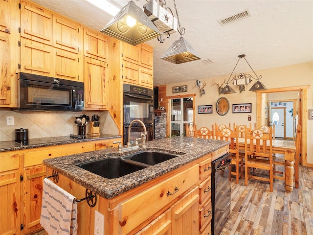 kitchen with visible vents, a center island with sink, a sink, decorative backsplash, and black appliances