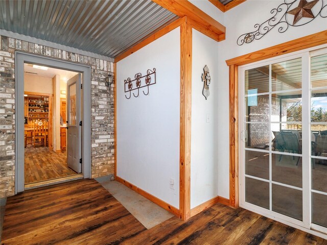 hall featuring baseboards, dark wood-style flooring, and brick wall