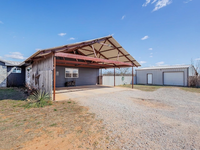 view of outdoor structure featuring a carport, an outdoor structure, driveway, and fence