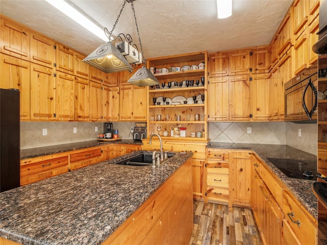 kitchen with open shelves, a kitchen island with sink, a sink, black appliances, and light wood-type flooring