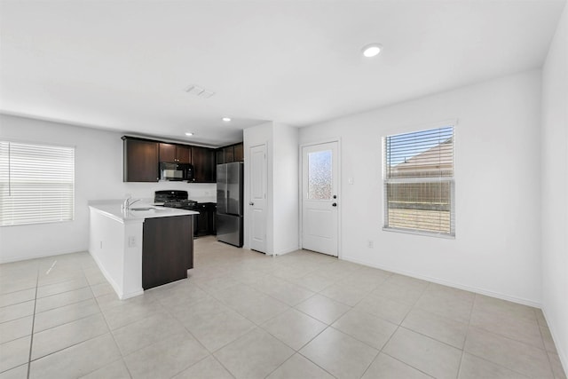 kitchen featuring black appliances, a healthy amount of sunlight, light countertops, and dark brown cabinetry