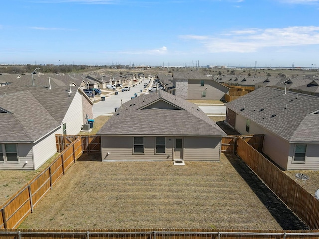 back of property featuring a yard, a residential view, a fenced backyard, and roof with shingles