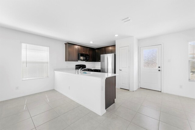 kitchen featuring dark brown cabinets, black microwave, light countertops, freestanding refrigerator, and a sink