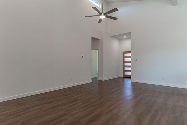 unfurnished living room with baseboards, dark wood-style flooring, a towering ceiling, and ceiling fan