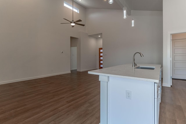 kitchen featuring a ceiling fan, an island with sink, dark wood-style flooring, a sink, and decorative light fixtures