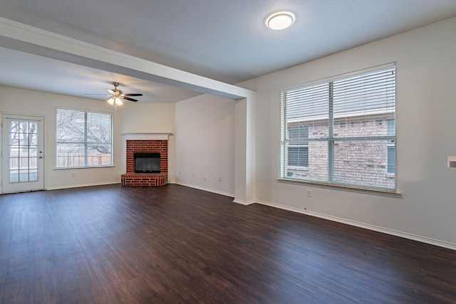 unfurnished living room with dark wood finished floors, ceiling fan, a brick fireplace, and baseboards