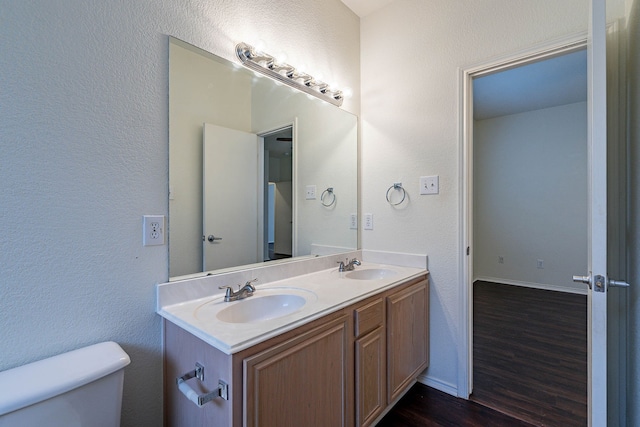 bathroom featuring double vanity, wood finished floors, toilet, and a sink