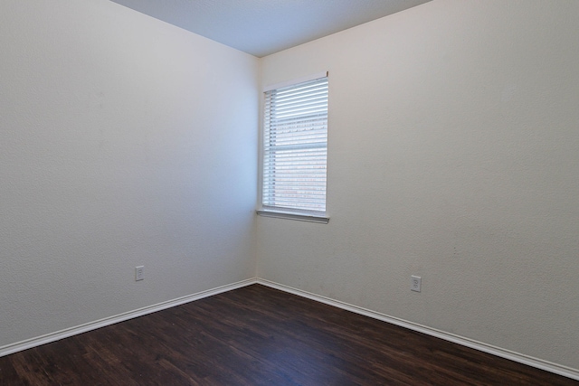 spare room featuring dark wood-type flooring and baseboards