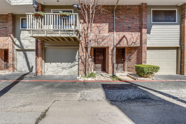 view of property featuring driveway, brick siding, a balcony, and an attached garage