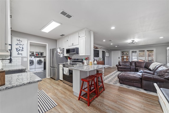 kitchen with visible vents, a sink, stainless steel appliances, light wood-style floors, and independent washer and dryer