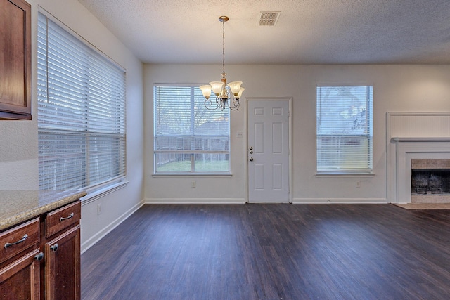 unfurnished dining area with visible vents, dark wood-type flooring, a fireplace with flush hearth, a notable chandelier, and a textured ceiling