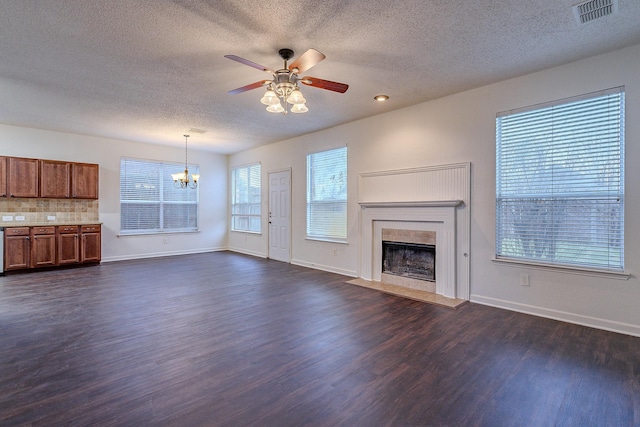 unfurnished living room featuring visible vents, a tiled fireplace, ceiling fan with notable chandelier, baseboards, and dark wood-style flooring