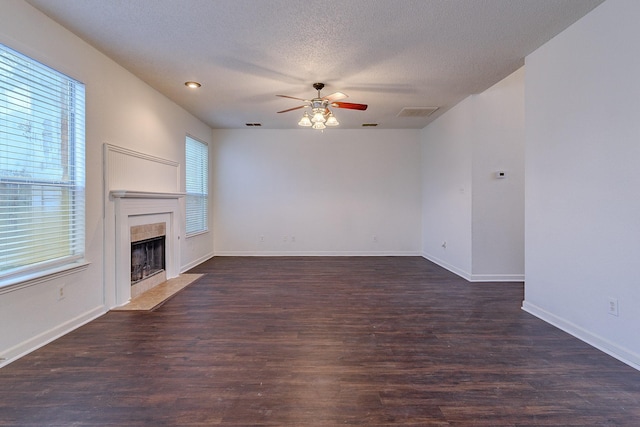 unfurnished living room featuring dark wood finished floors, a ceiling fan, a wealth of natural light, and a tile fireplace