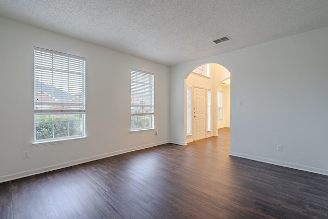 empty room featuring dark wood finished floors, plenty of natural light, visible vents, and arched walkways