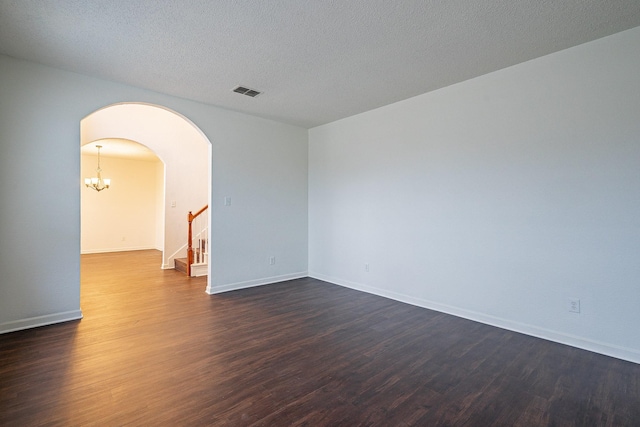 unfurnished room with visible vents, stairway, arched walkways, dark wood-style floors, and a notable chandelier