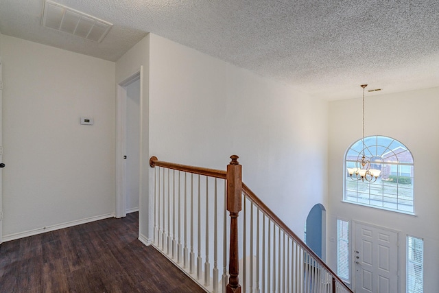 corridor featuring wood finished floors, baseboards, visible vents, a textured ceiling, and a chandelier