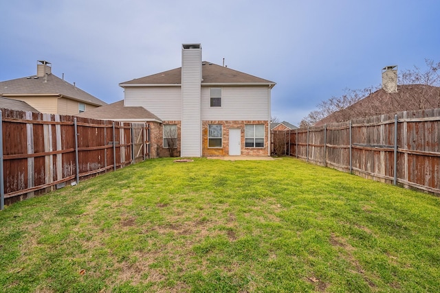 back of house with a lawn, brick siding, a fenced backyard, and a chimney