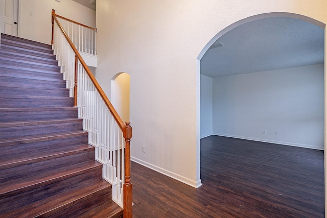 staircase featuring wood finished floors, baseboards, and arched walkways