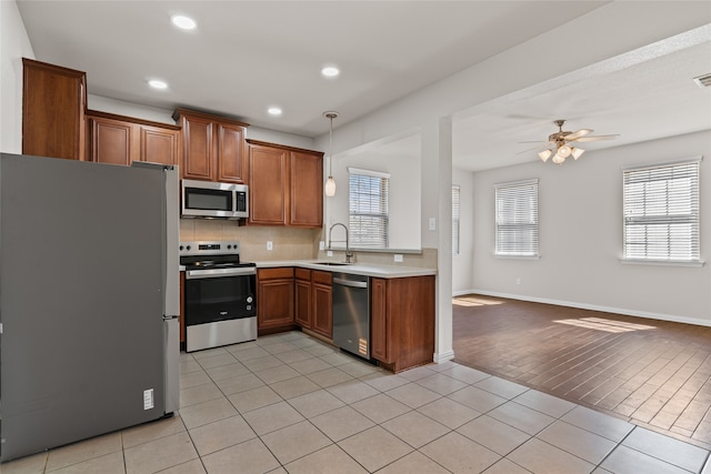 kitchen featuring open floor plan, light tile patterned floors, brown cabinetry, stainless steel appliances, and a sink