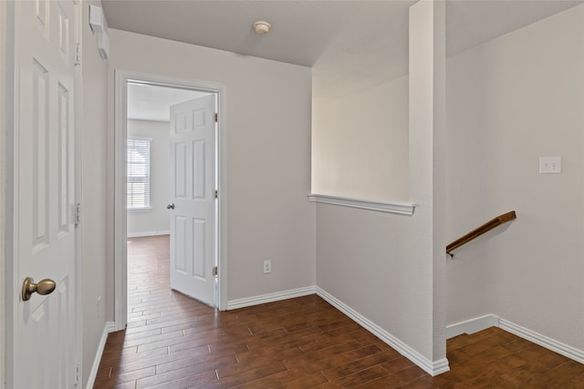 corridor featuring an upstairs landing, dark wood-type flooring, and baseboards