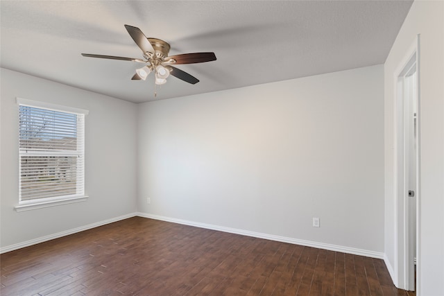 empty room with dark wood finished floors, a ceiling fan, and baseboards