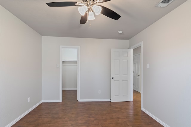 unfurnished bedroom with visible vents, a walk in closet, baseboards, and dark wood-style flooring