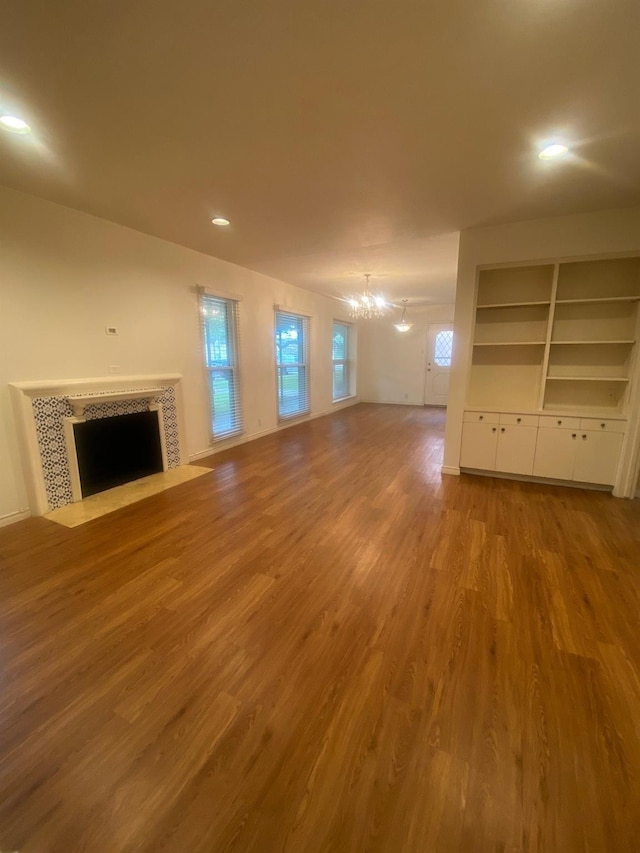 unfurnished living room featuring a notable chandelier, a healthy amount of sunlight, wood finished floors, and a tile fireplace