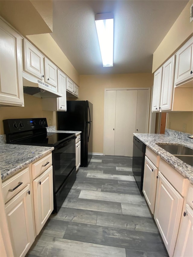 kitchen with light stone countertops, under cabinet range hood, wood finished floors, a textured ceiling, and black appliances