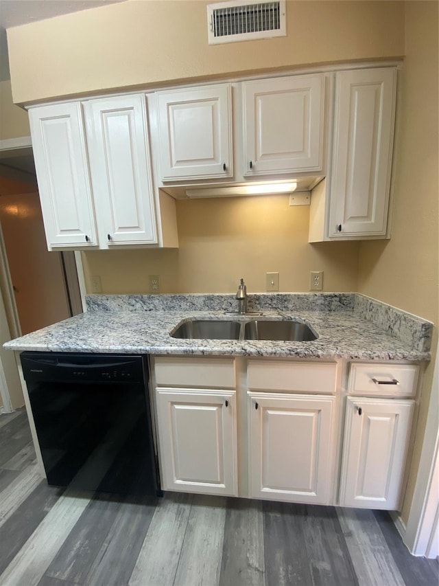 kitchen featuring visible vents, black dishwasher, light stone counters, light wood-style flooring, and a sink