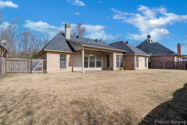 rear view of property featuring brick siding, ceiling fan, a lawn, a chimney, and a fenced backyard