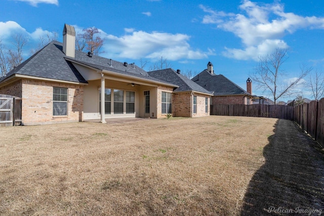 back of property with brick siding, ceiling fan, a chimney, a yard, and a fenced backyard