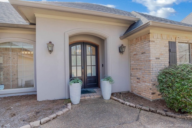 entrance to property with french doors, brick siding, roof with shingles, and stucco siding