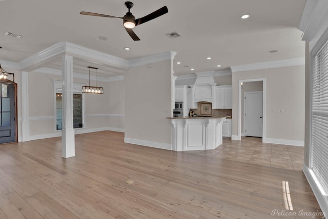 unfurnished living room featuring light wood finished floors, visible vents, baseboards, decorative columns, and ceiling fan with notable chandelier