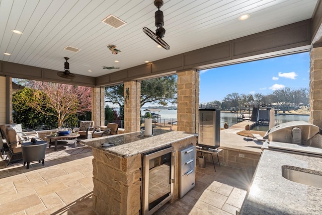 view of patio with visible vents, a water view, beverage cooler, outdoor wet bar, and exterior kitchen