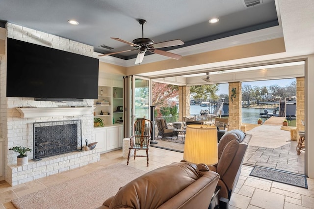 living room with visible vents, a brick fireplace, ceiling fan, stone tile floors, and a raised ceiling