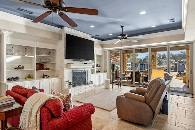 living area with a tray ceiling, stone tile floors, crown molding, and visible vents