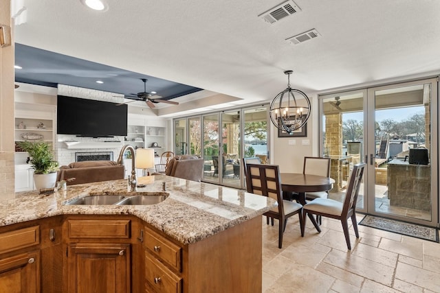 kitchen with a raised ceiling, brown cabinetry, visible vents, and a sink